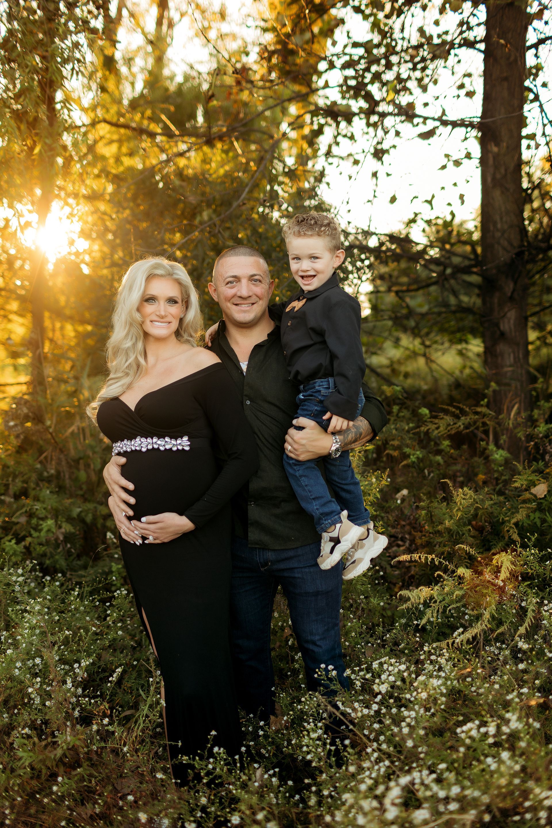 A pregnant woman , a man and a child are posing for a picture in the woods.