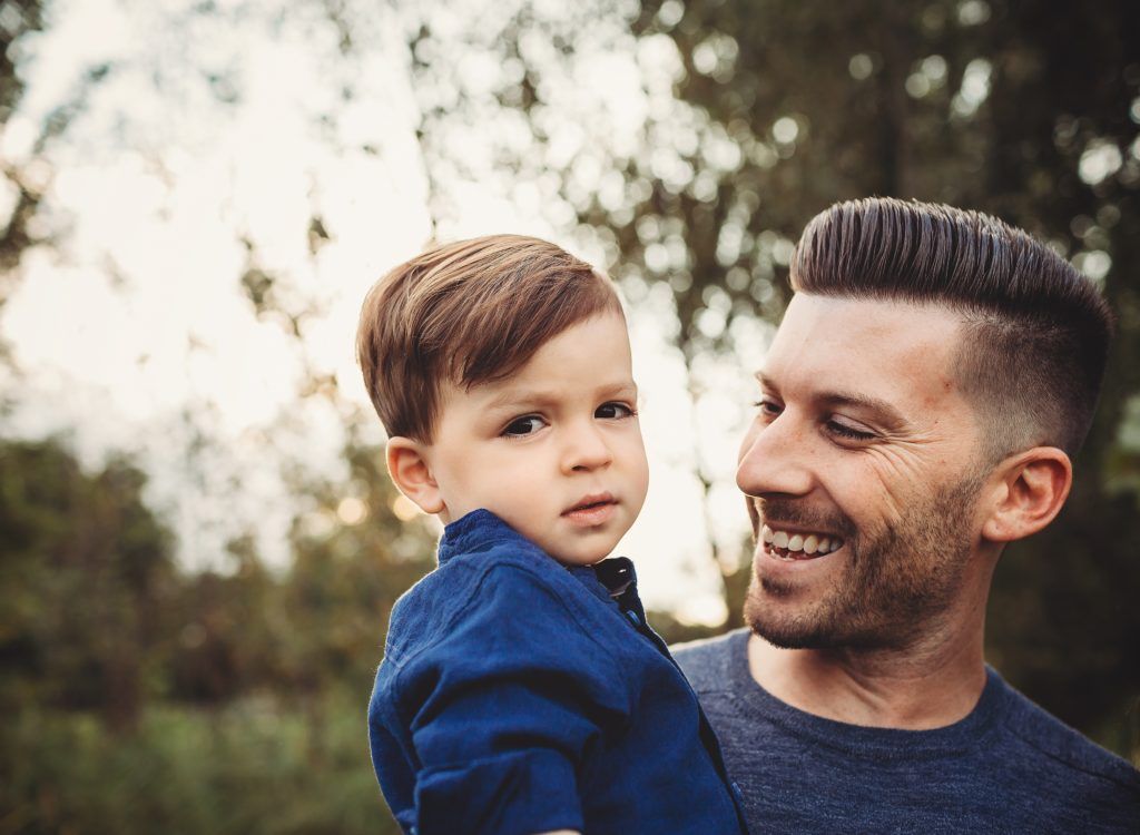 A man is holding a baby boy in his arms and smiling.