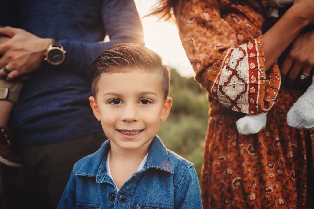 A young boy is standing in front of a woman holding a baby.