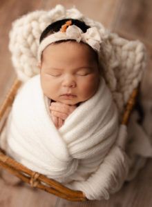 A newborn baby wrapped in a white blanket is sleeping in a wicker basket.