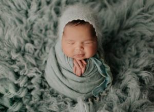 A newborn baby is wrapped in a blanket and wearing a hat.