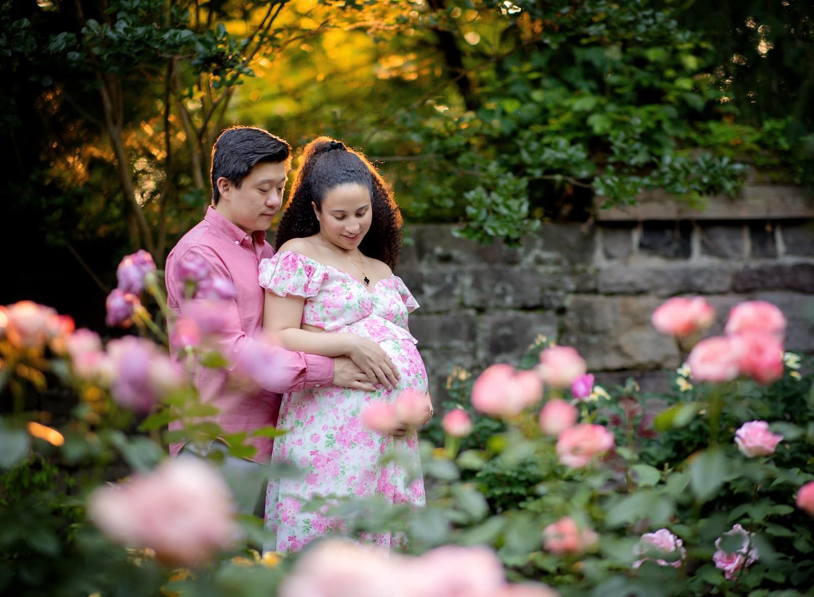 Expecting parents during a spring maternity photography session surrounded by pink flowers in Bergen County, NJ.