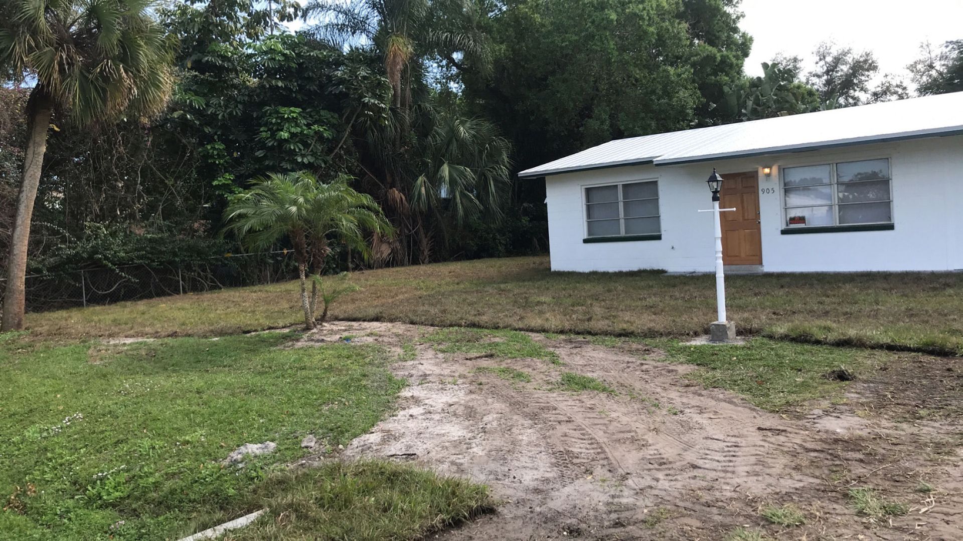 A white house with a dirt road leading to it is surrounded by trees.