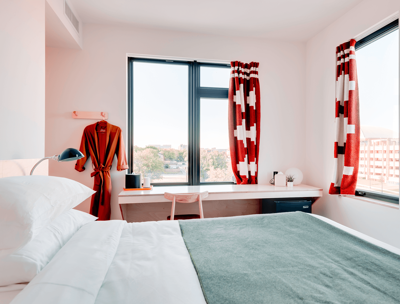 A bedroom with a bed , desk , and window with a robe hanging on the wall.