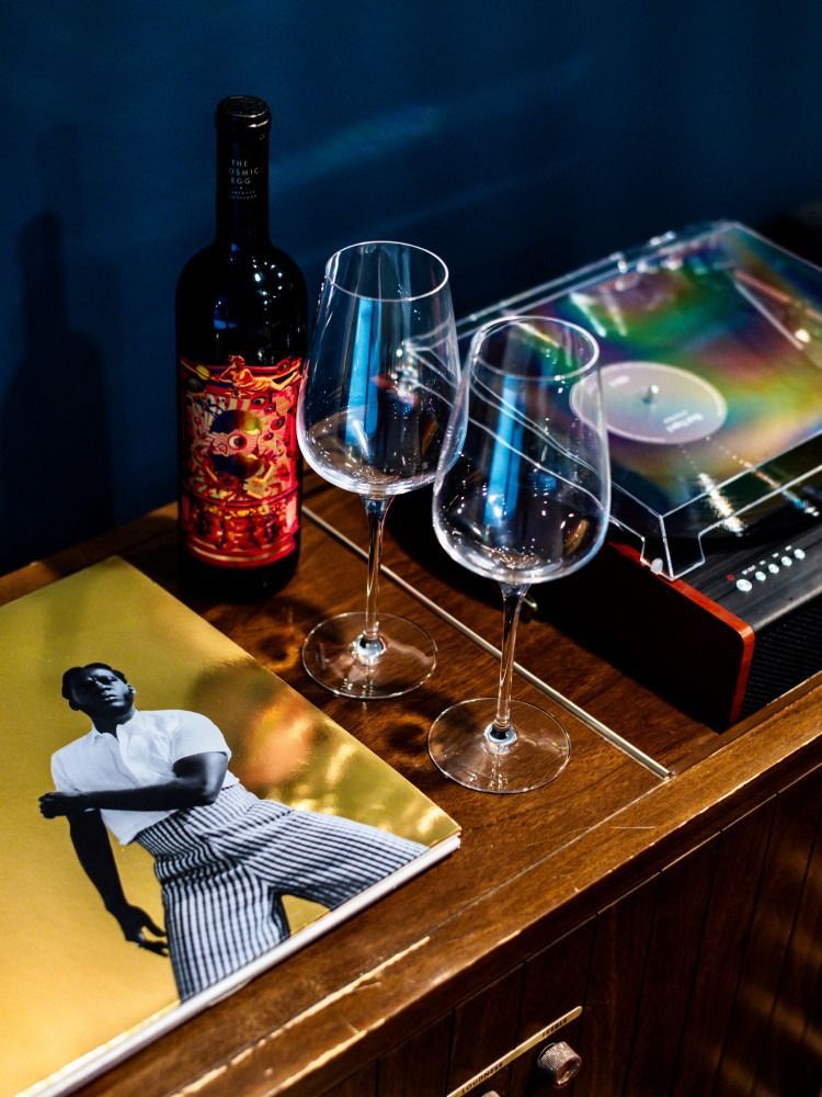 A bottle of wine and two wine glasses are on a table next to a record player.