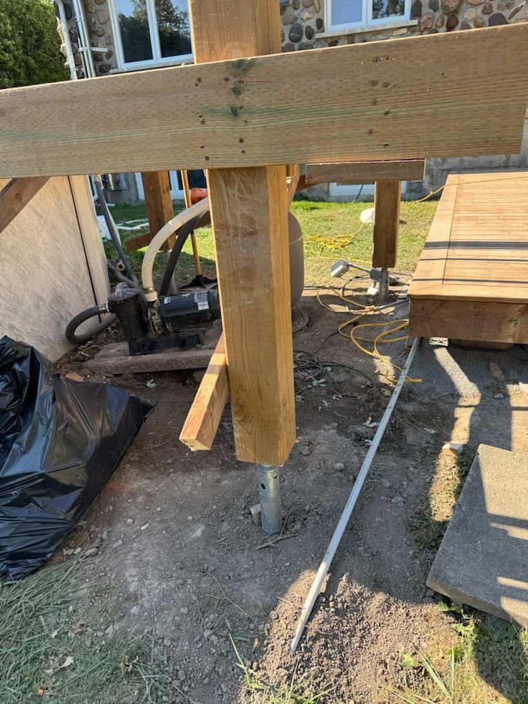 Sur un chantier, un poteau de soutien de terrasse en bois est renforcé par une équerre métallique.