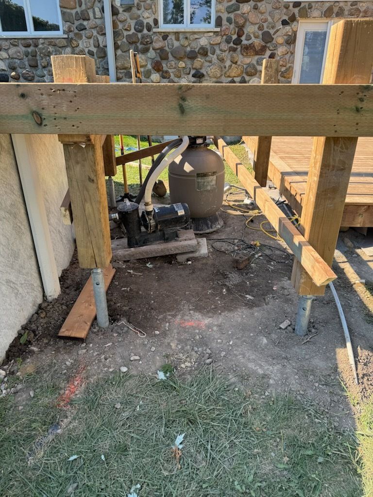 Cadre de support de terrasse en bois avec une bonbonne de propane et des outils à côté d'une maison en pierre.