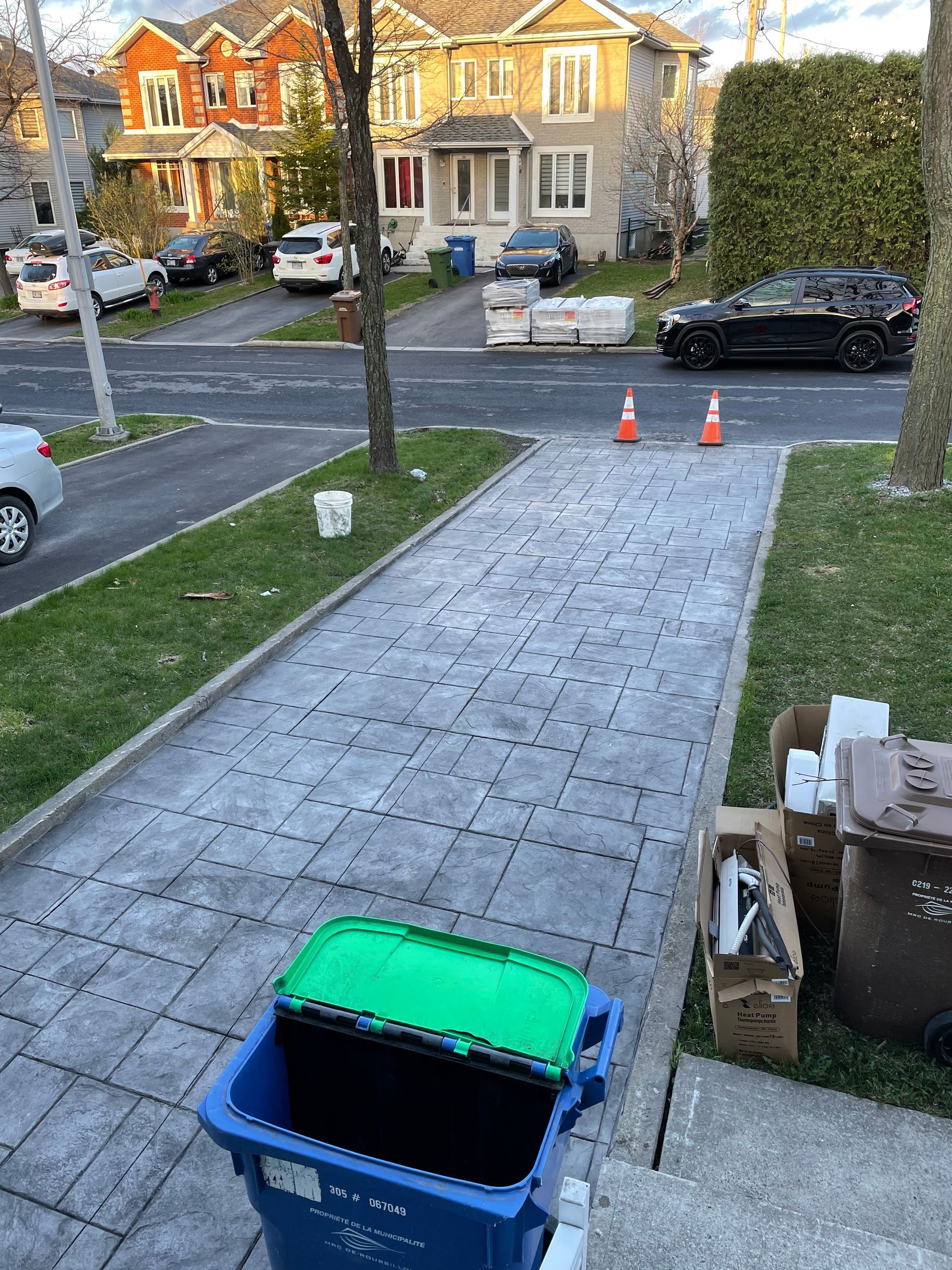 Une poubelle bleue avec un couvercle vert se trouve sur un trottoir.