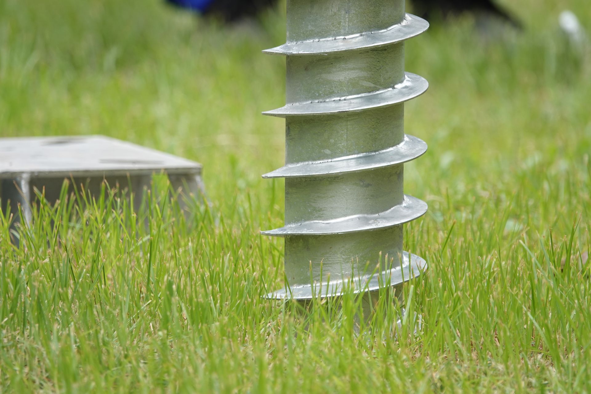 Vis métallique plantée dans l'herbe verte, à proximité d'un petit bloc de béton.