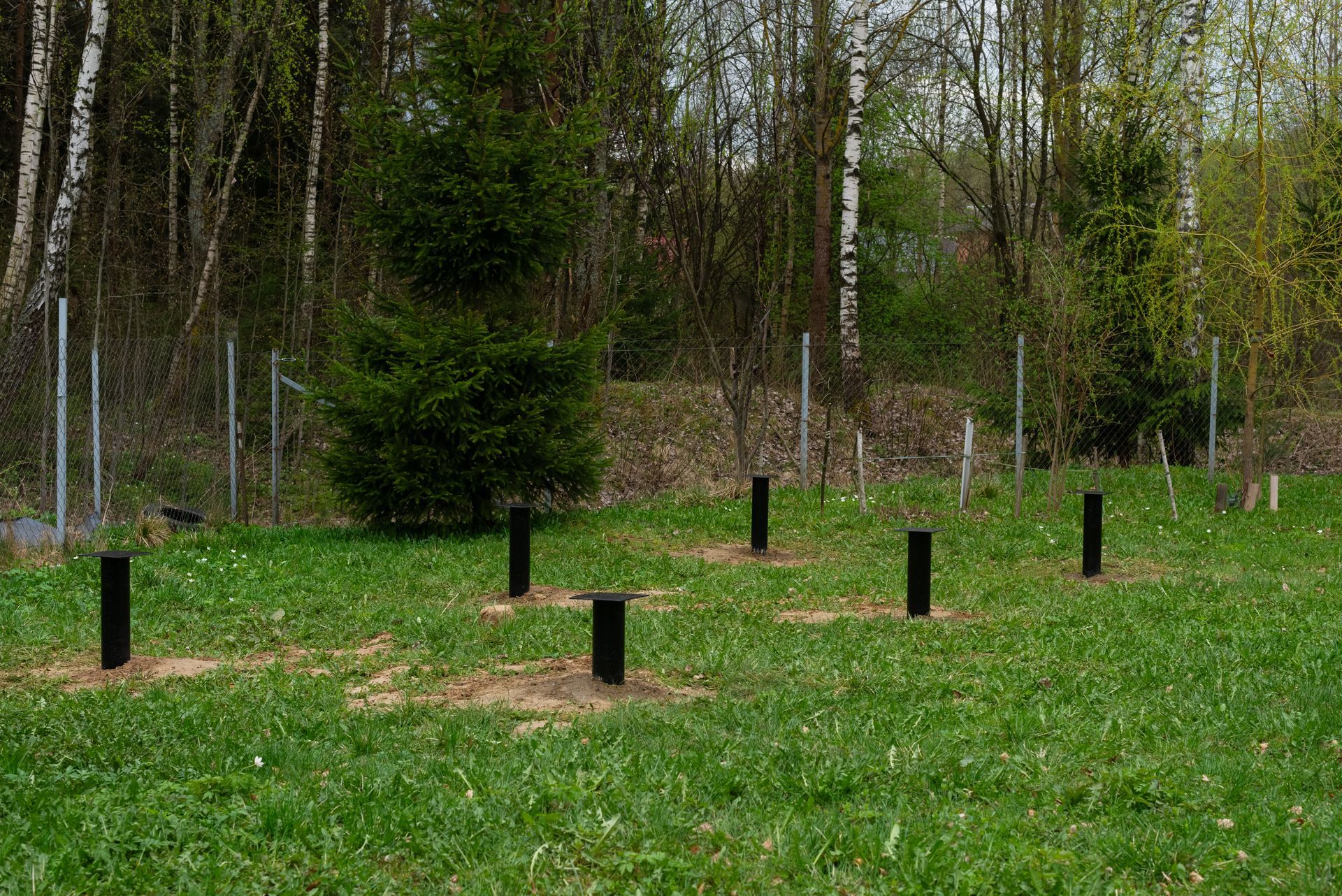 Des poteaux noirs dans un champ herbeux, près d'une clôture en grillage et d'arbres