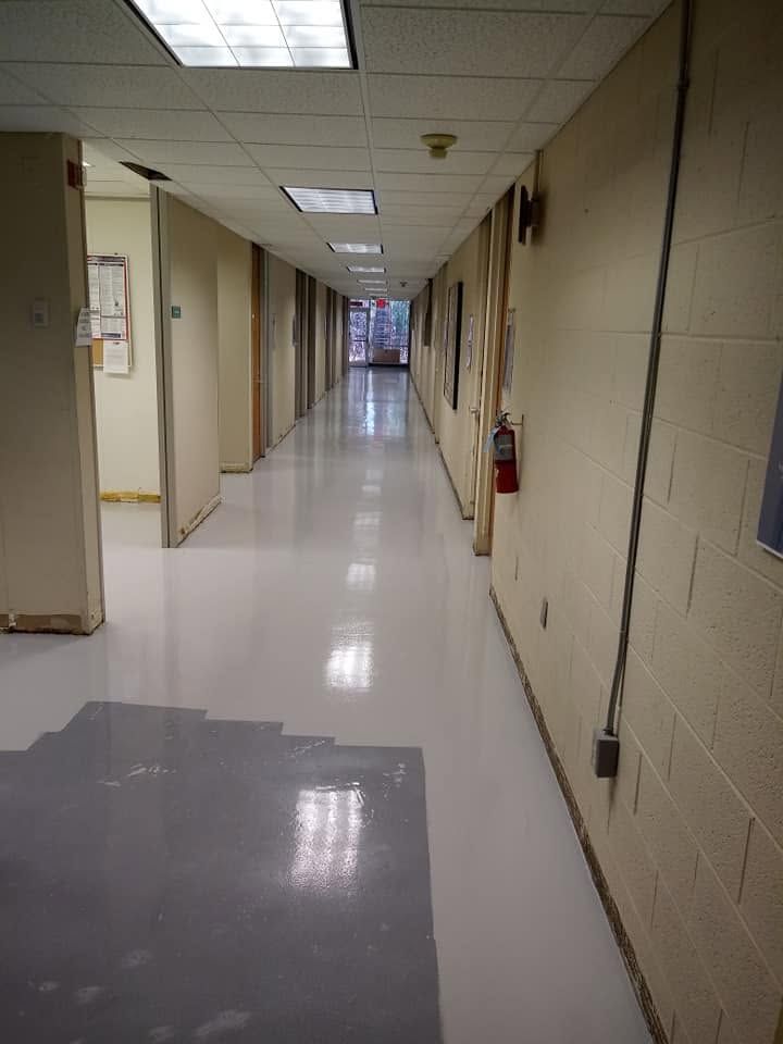 Empty beige hallway with white tiled floor, fluorescent lights, and doors along both sides