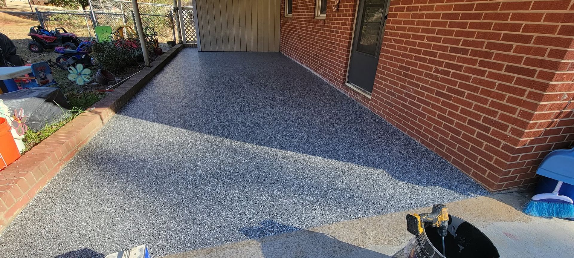Freshly poured gray gravel path beside a brick house, with a garden border on the left.