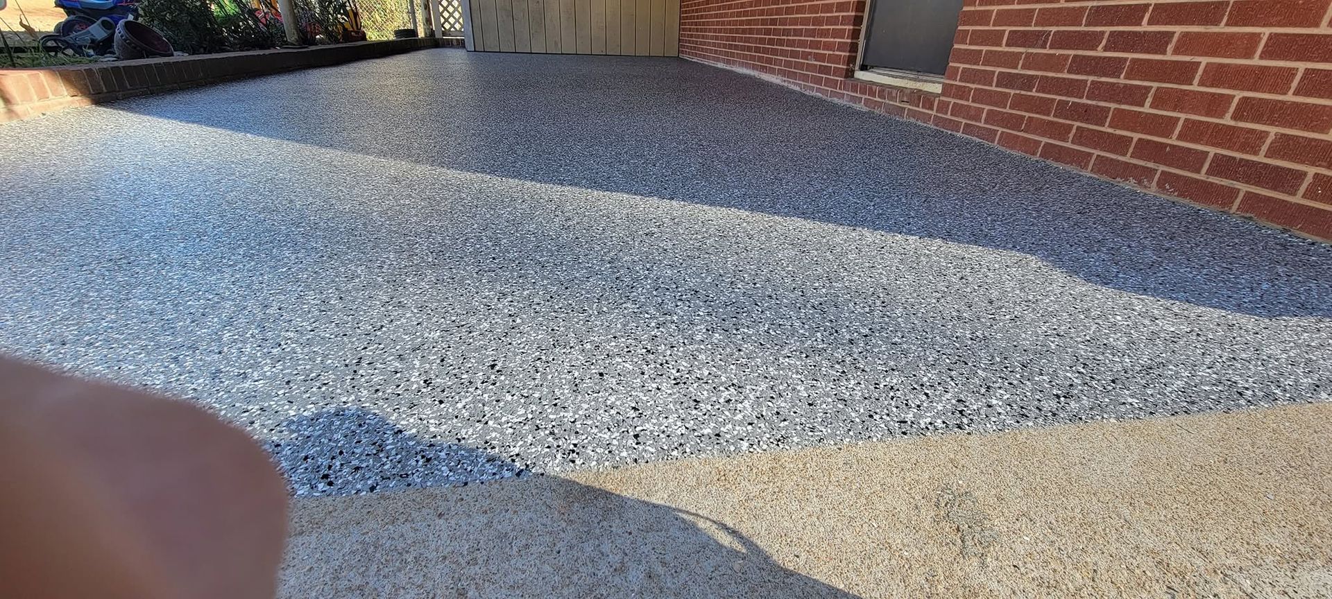 Gravel driveway beside a brick house, with a concrete edge and a small shadow in the foreground