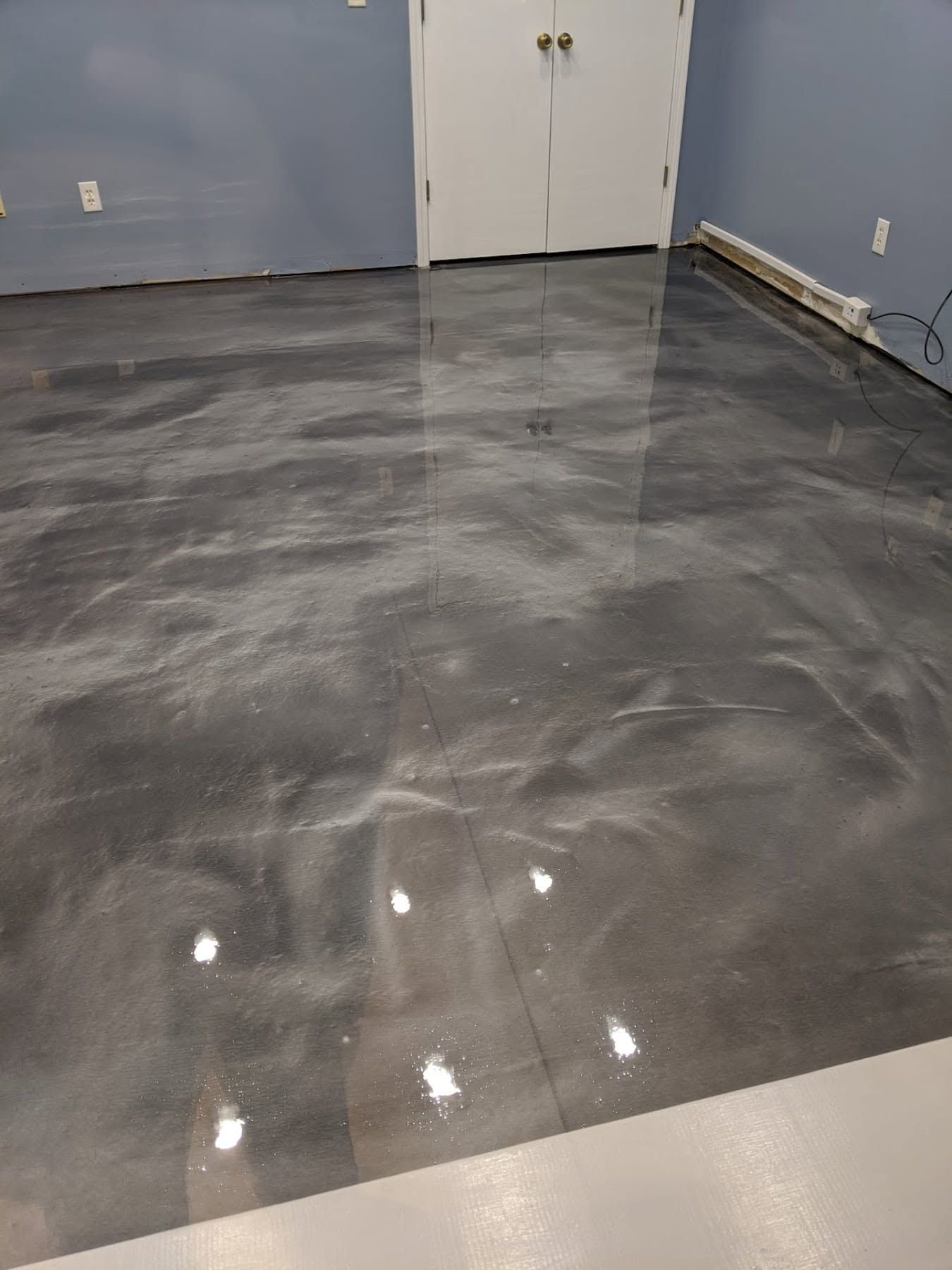 Empty room with glossy gray concrete floor and blue walls, reflecting ceiling lights.