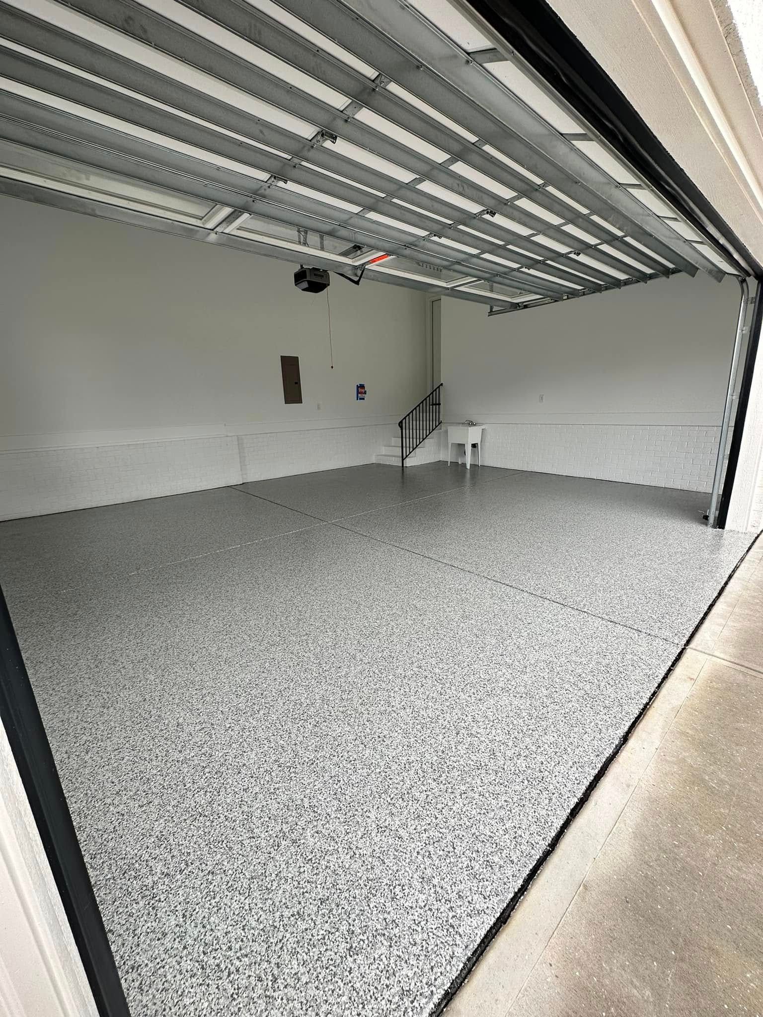 Empty garage interior with speckled floor, open door, and a small table near the back wall