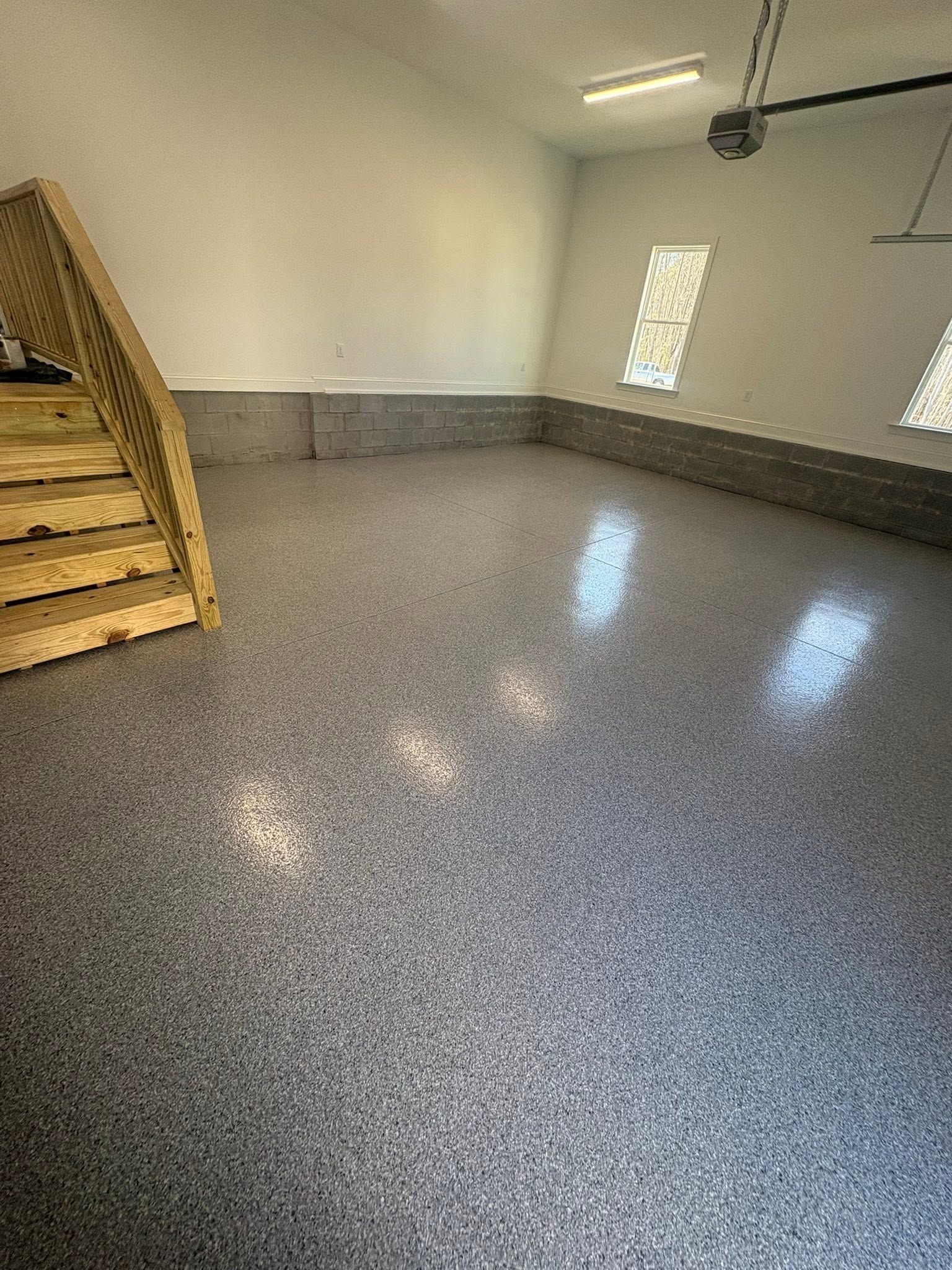 Empty garage with speckled epoxy floor, white walls, wooden stairs, and small windows.