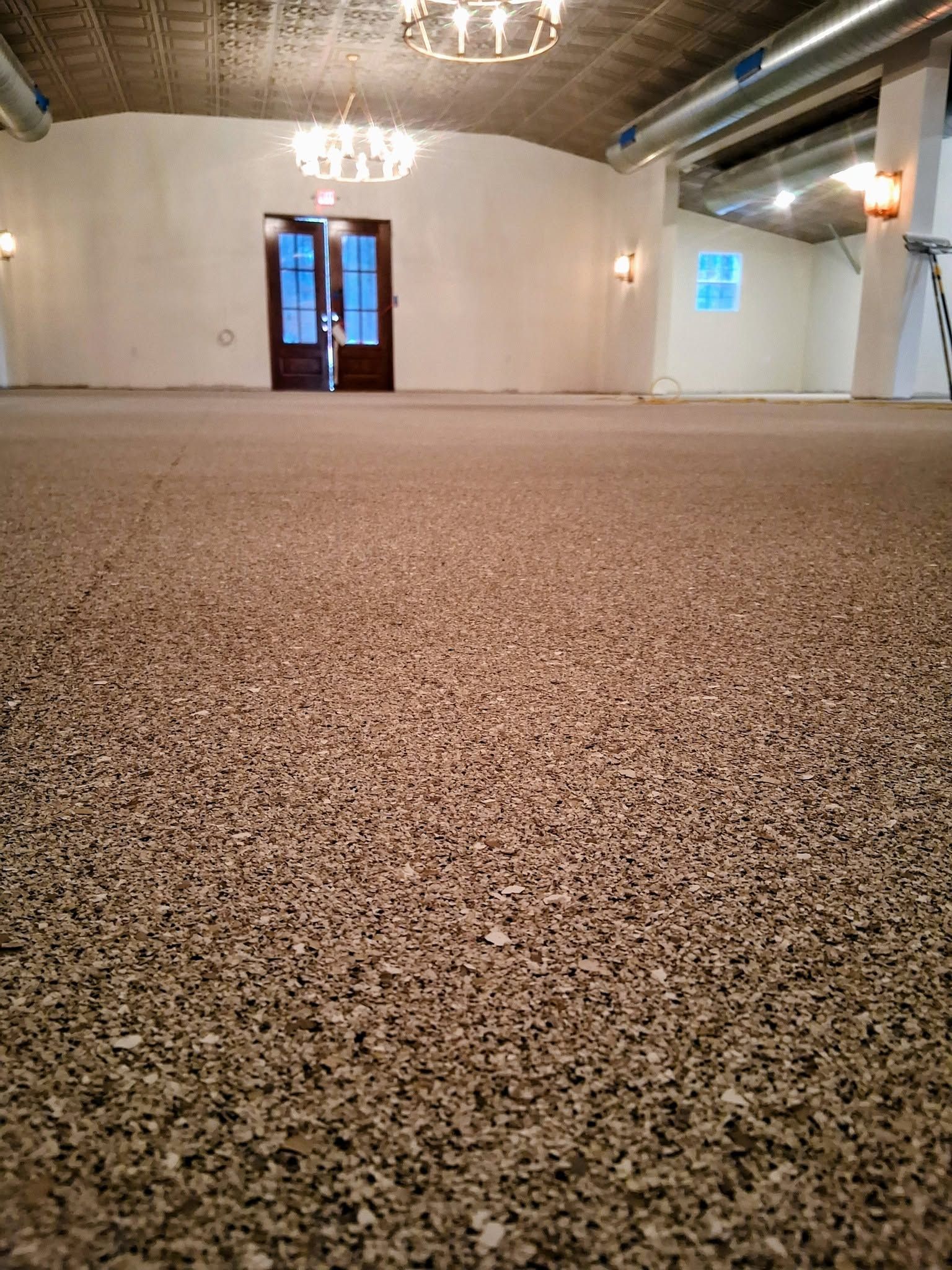 Empty indoor hall with speckled flooring, white walls, chandeliers, and double doors at the far end