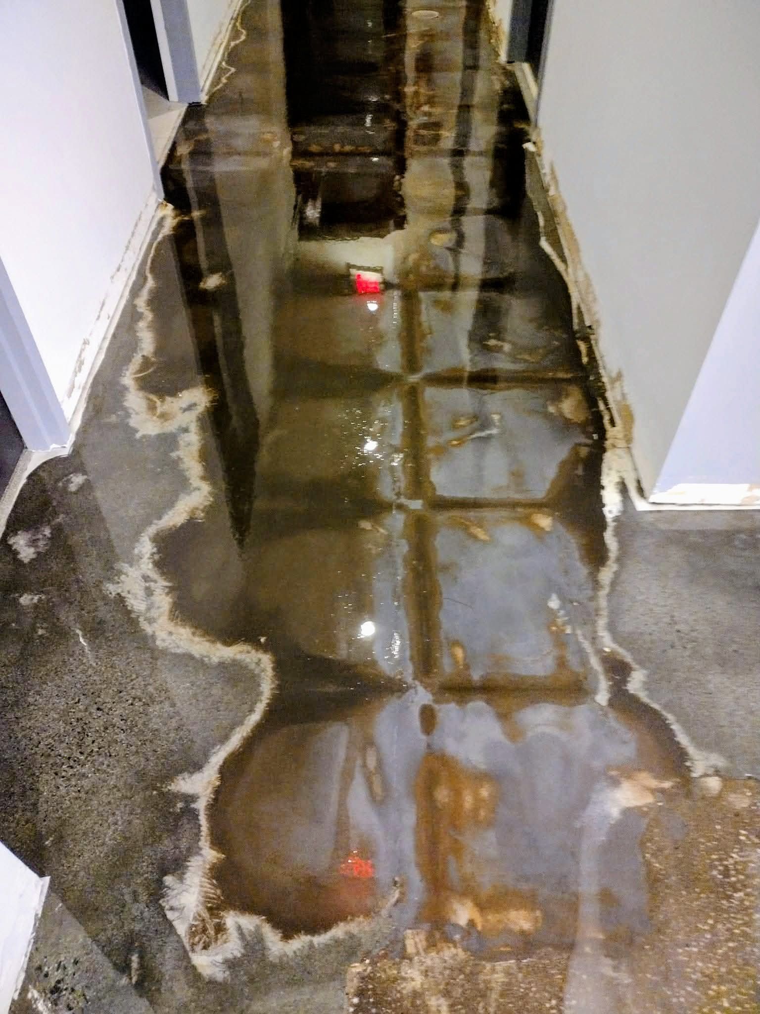 Flooded hallway with standing water reflecting light and debris on the floor