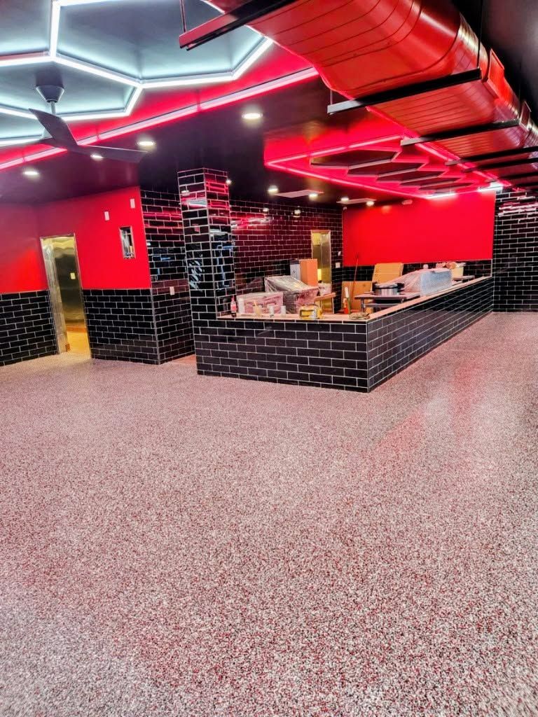 Empty arcade or entertainment space with red walls, black counters, and patterned carpet under neon ceiling lights