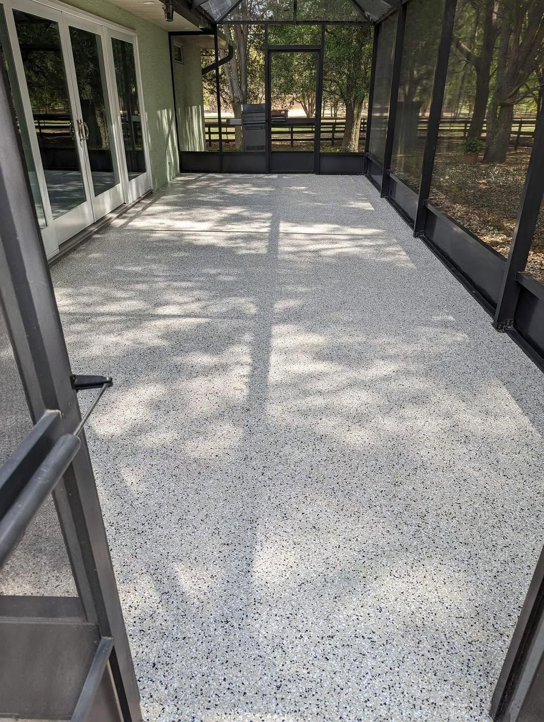 Screened porch with speckled concrete floor, black railings, and trees visible outside
