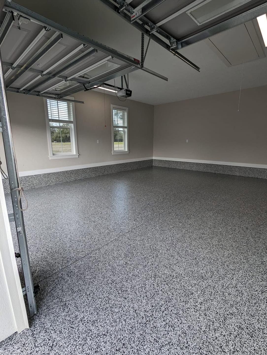 Empty garage with gray epoxy floor, open overhead door, and two small windows on the back wall