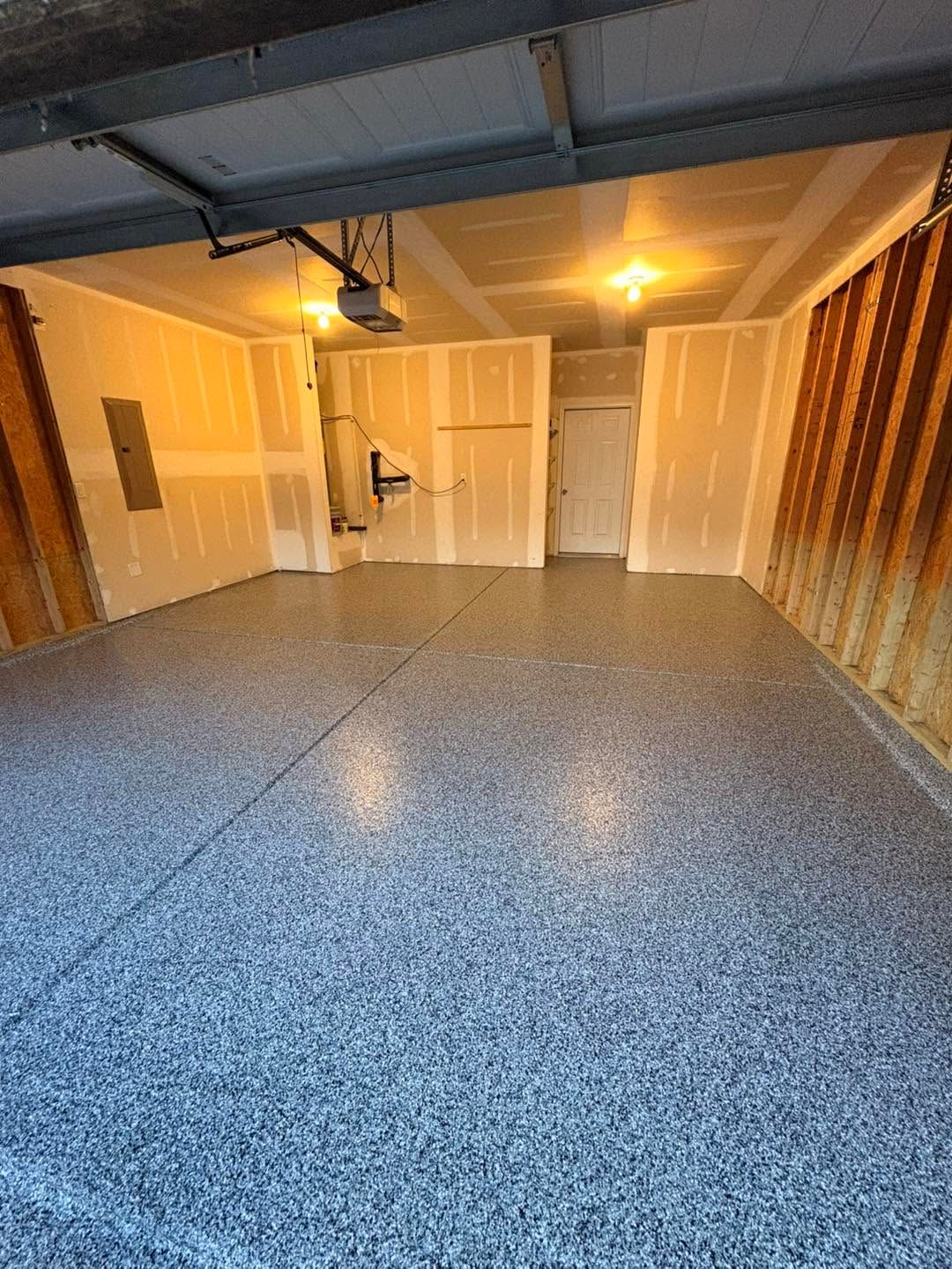 Empty garage with blue speckled floor, open white doors, and warm overhead light at the back.