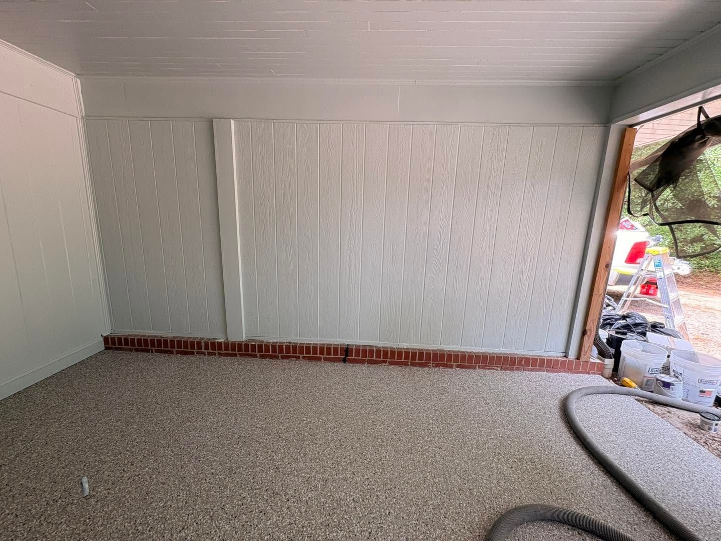 Empty living room with white paneled walls, carpeted floor, and a brick hearth by a window.