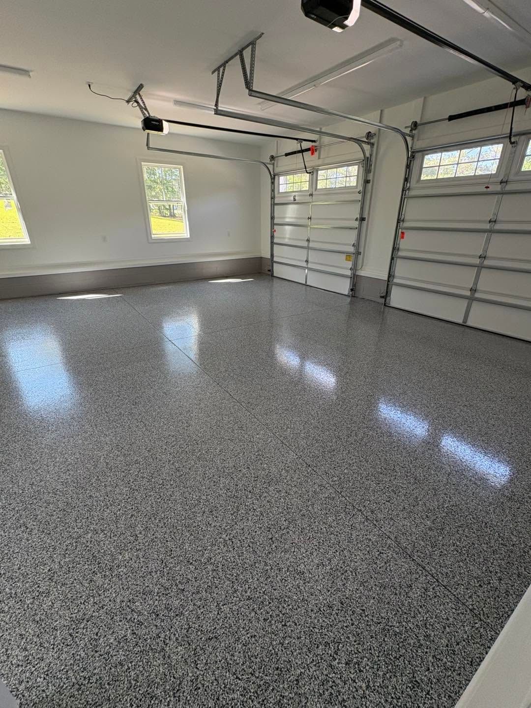 Empty two-car garage with speckled floor, white walls, windows, and closed overhead door.