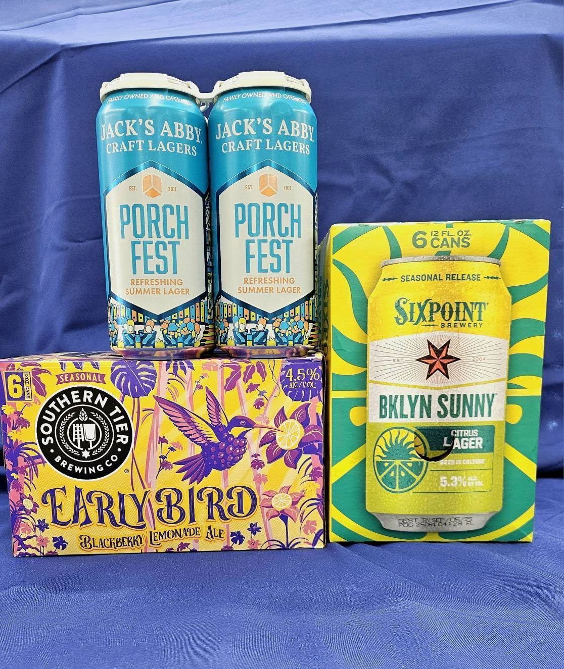 Assorted craft beer six-packs in colorful packaging on a blue cloth backdrop