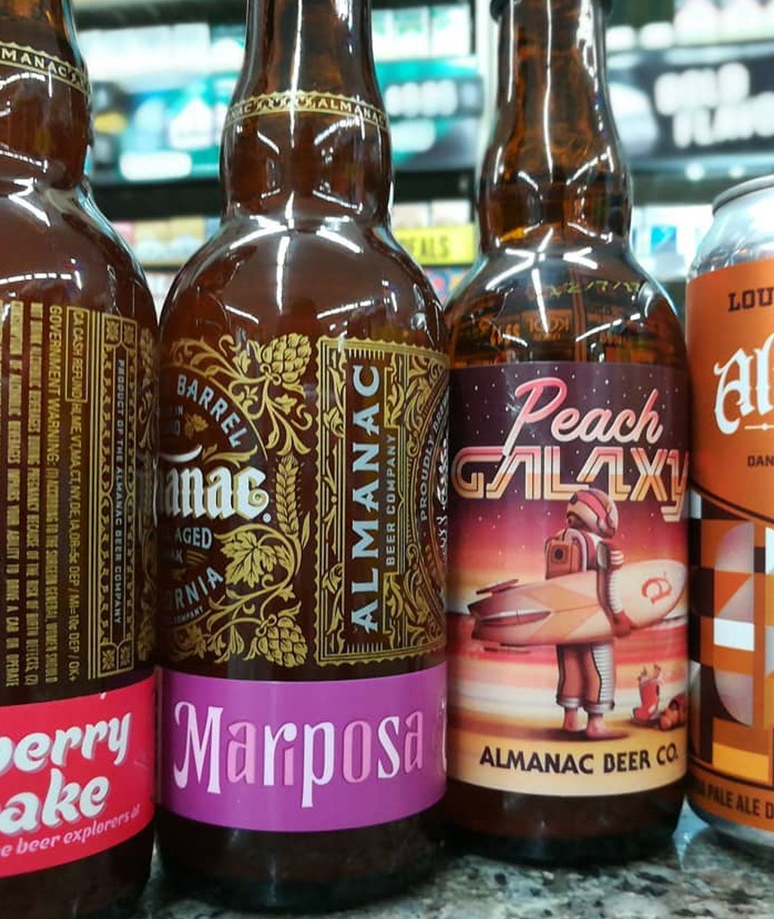 Row of colorful craft beer bottles with labels including Marposa and Peach Galaxy on a store shelf