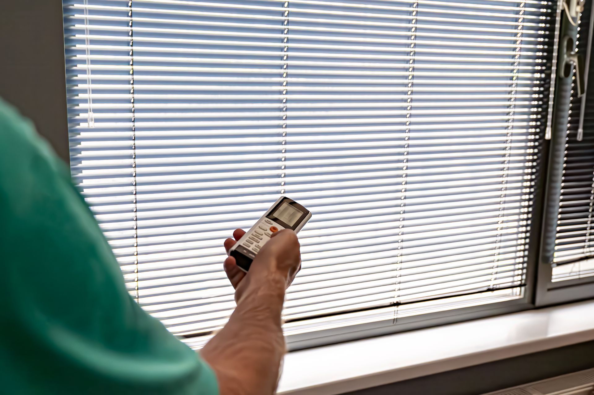 Someone using a remote to control their window blinds 