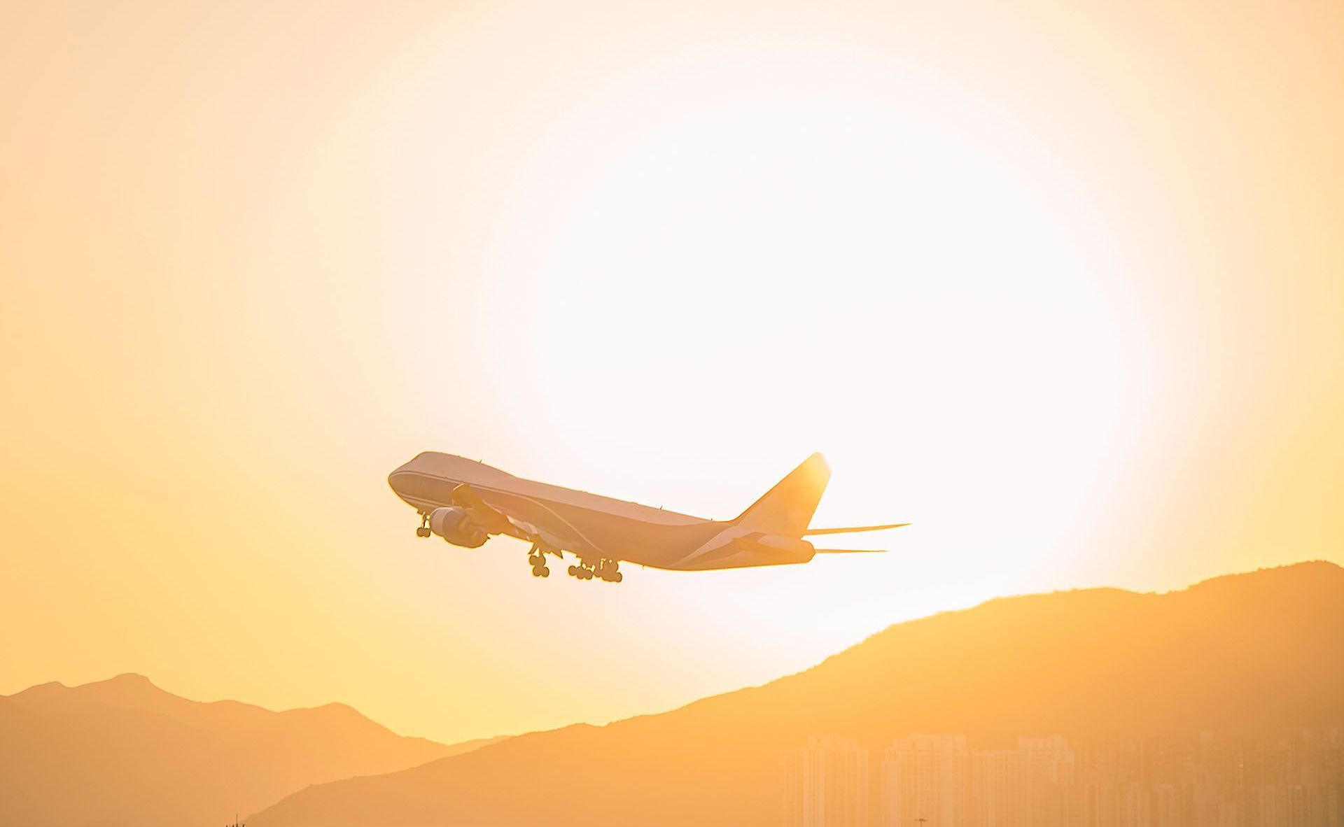 Airplane taking off against a bright, orange sunset; mountains in the background.