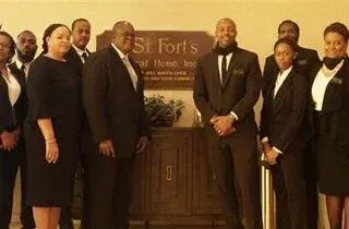 Group of seven people in dark formal attire standing in front of a St. Forts funeral home sign.