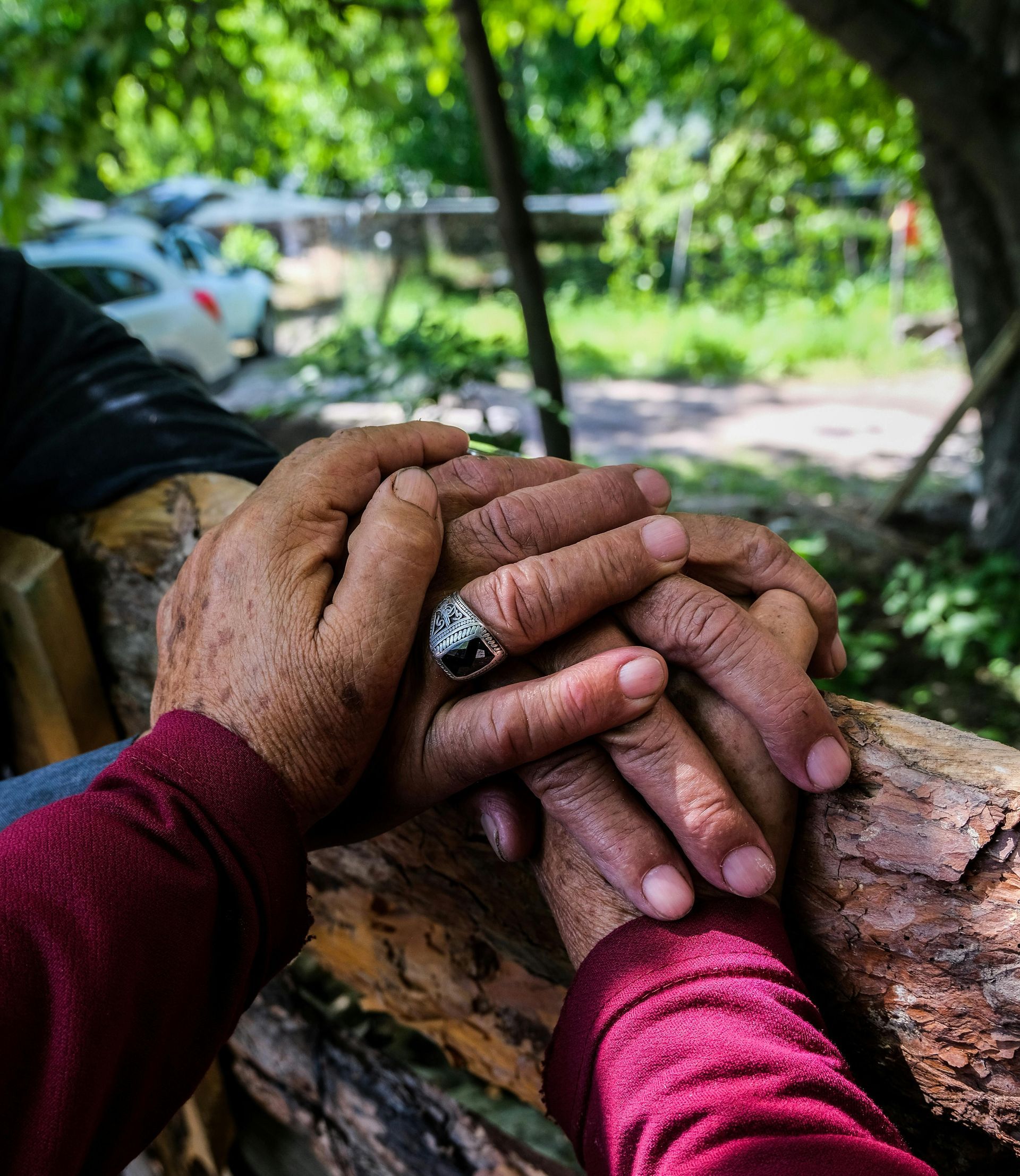 Two hands in red sleeves clasped together on a wooden bench outdoors