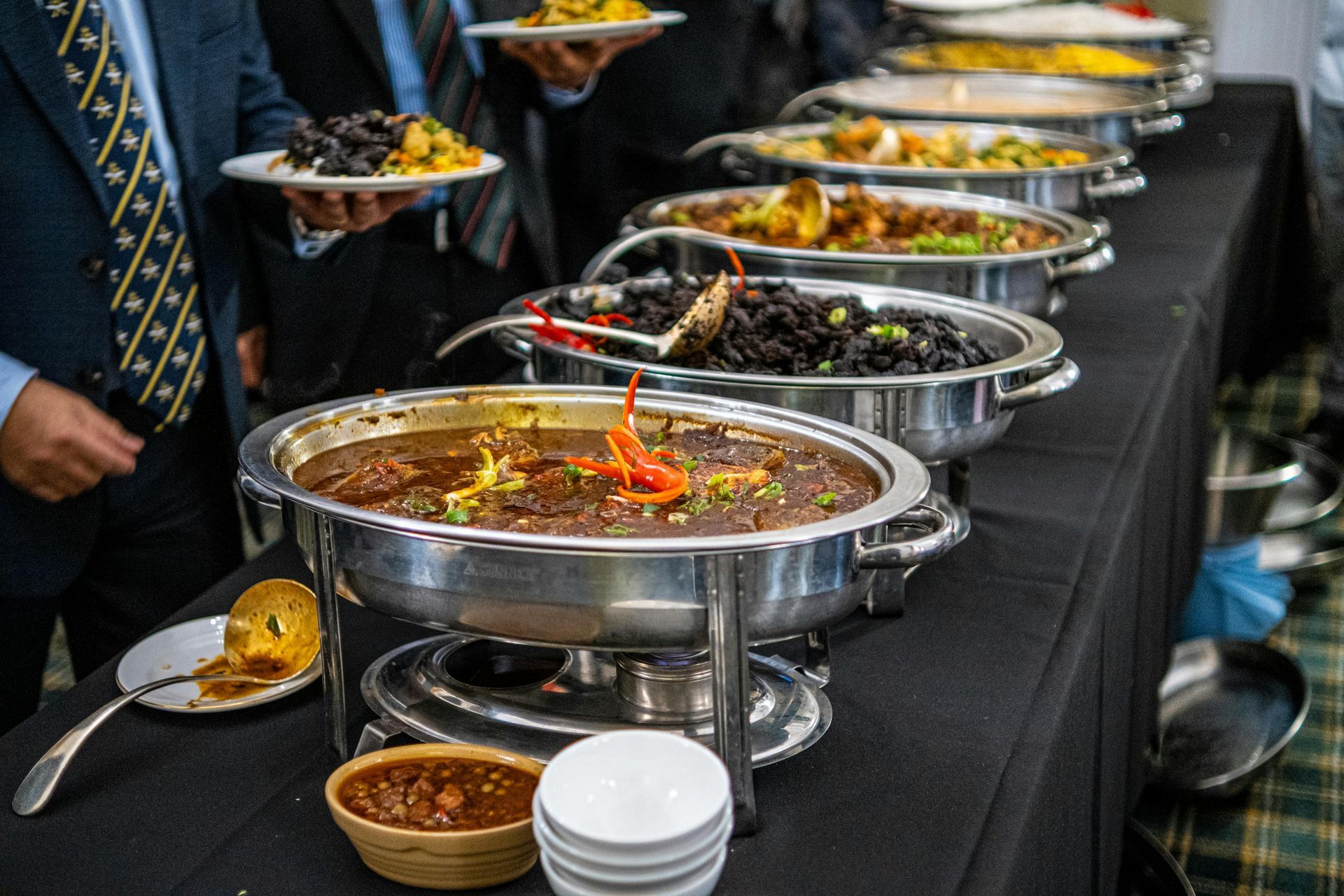 Buffet line with metal serving trays of assorted hot dishes on a black tablecloth
