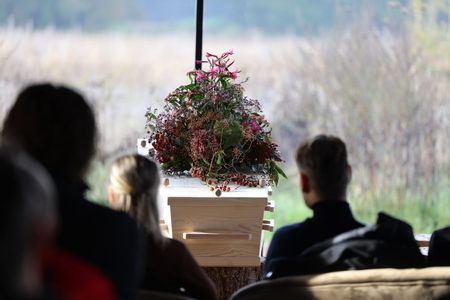Audience seated facing a flower arrangement on a podium in a bright indoor setting