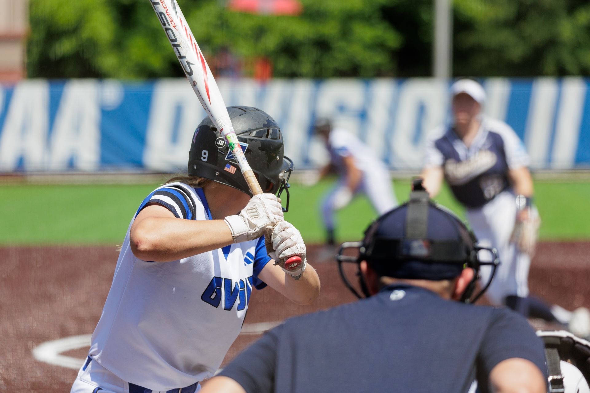 Baseball batter in white swings at a pitch, with catcher and umpire behind home plate.