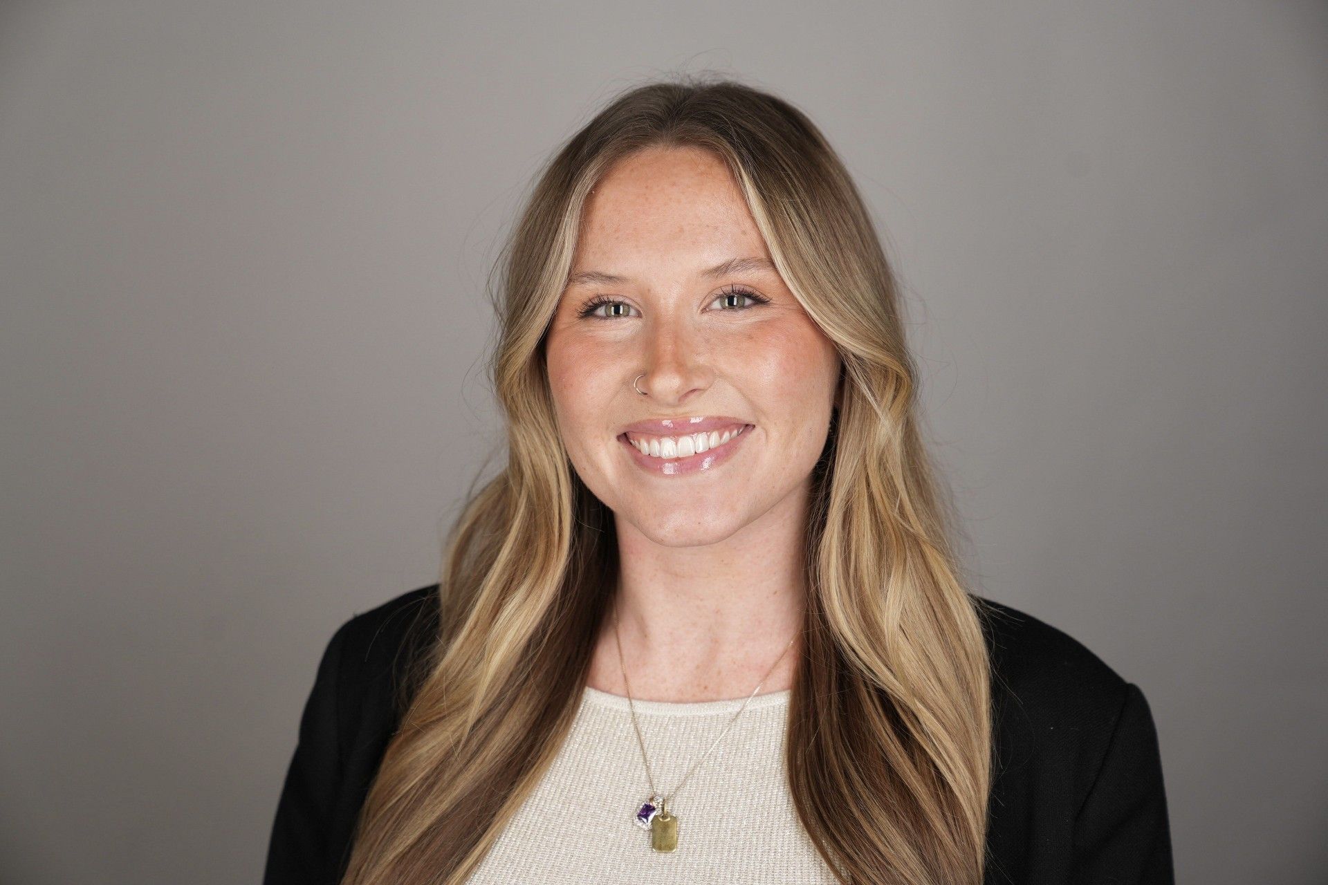 Smiling person in a black blazer and white top against a gray background