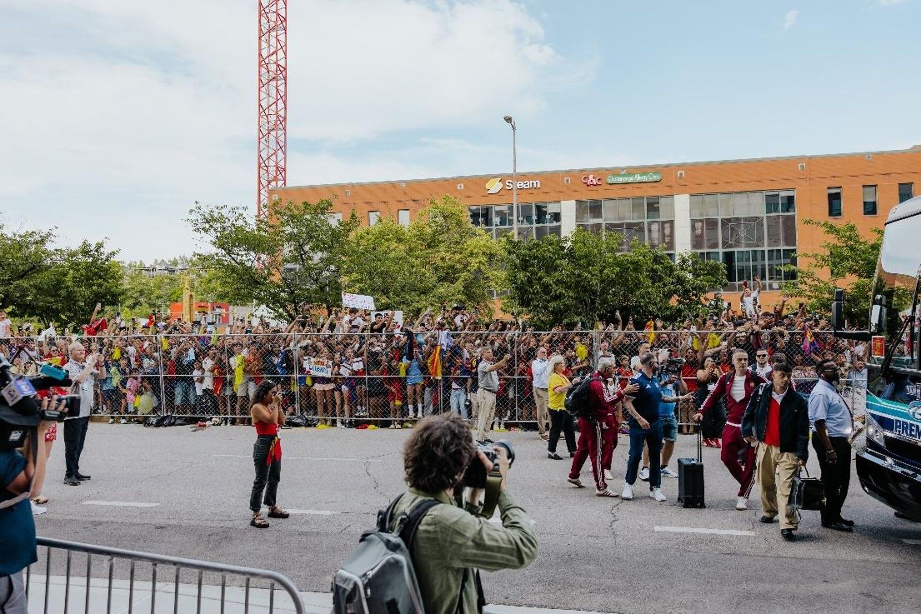 Crowd gathered behind barriers at an outdoor event near a brick building, with a photographer in the foreground