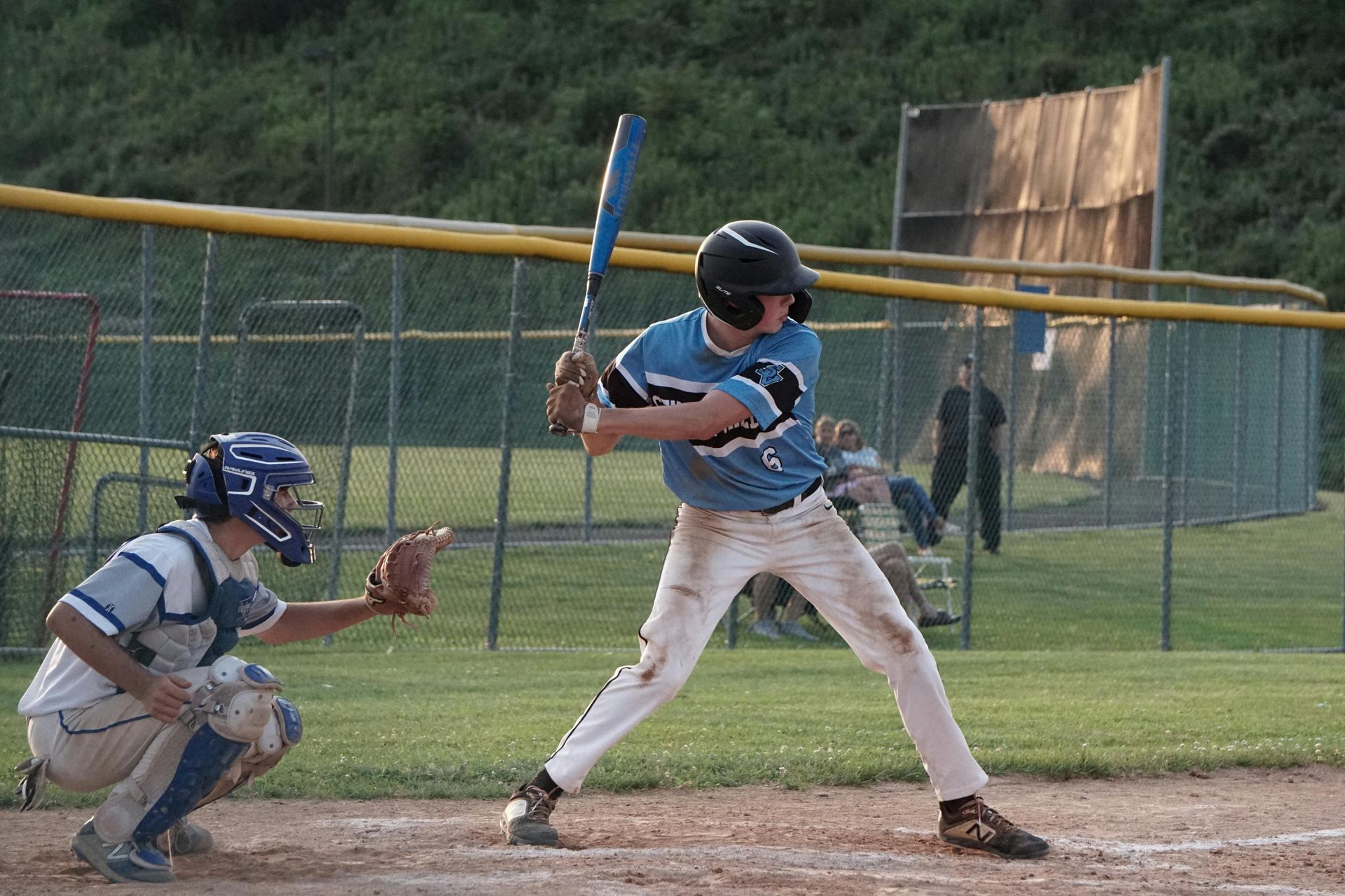 Baseball batter in blue prepares to swing as catcher crouches behind home plate.