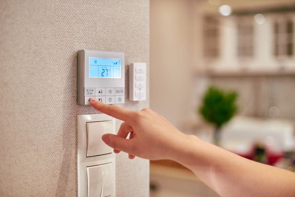 A Person is Pressing a Button on a Thermostat — Rabbit Electrical Service In Taminda, NSW