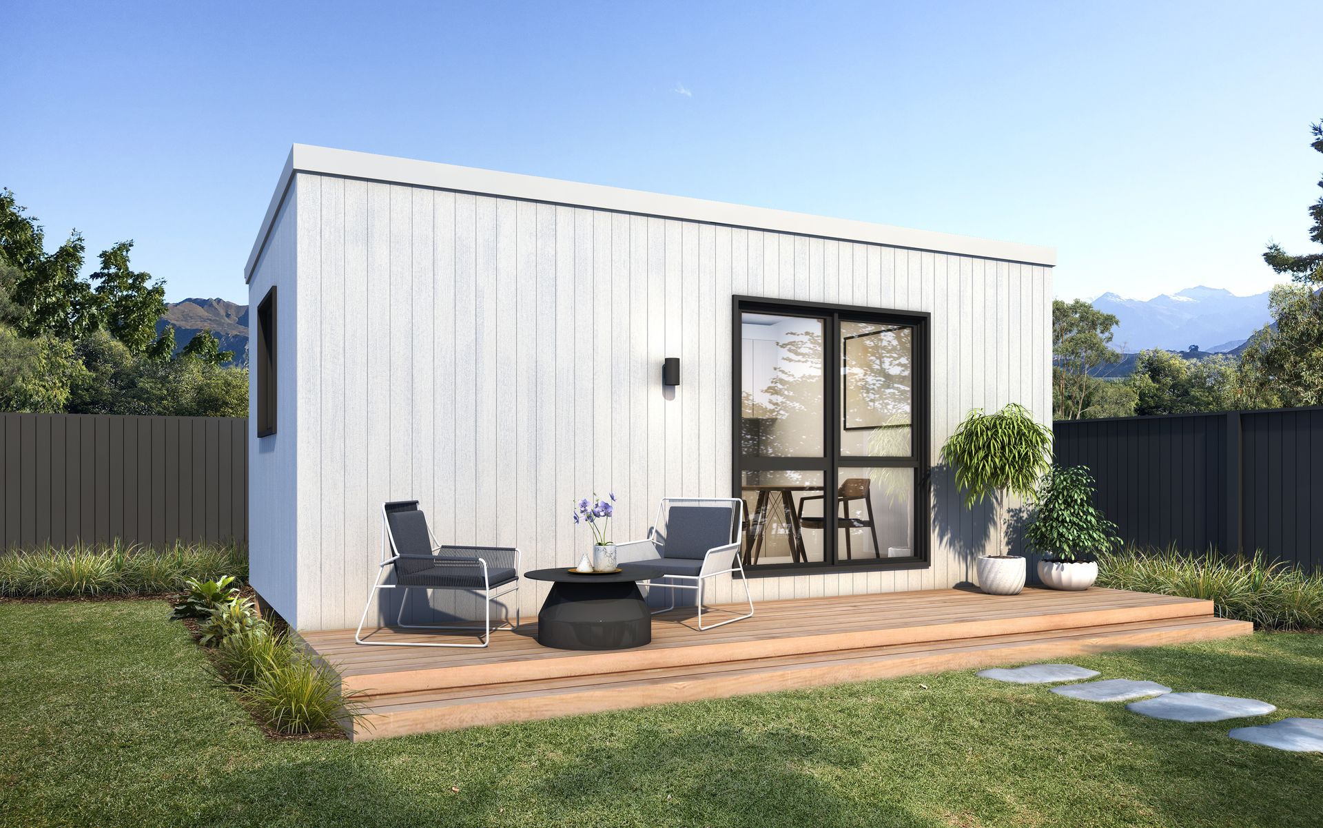 Small white modern cabin with patio furniture and potted plants in a grassy backyard.