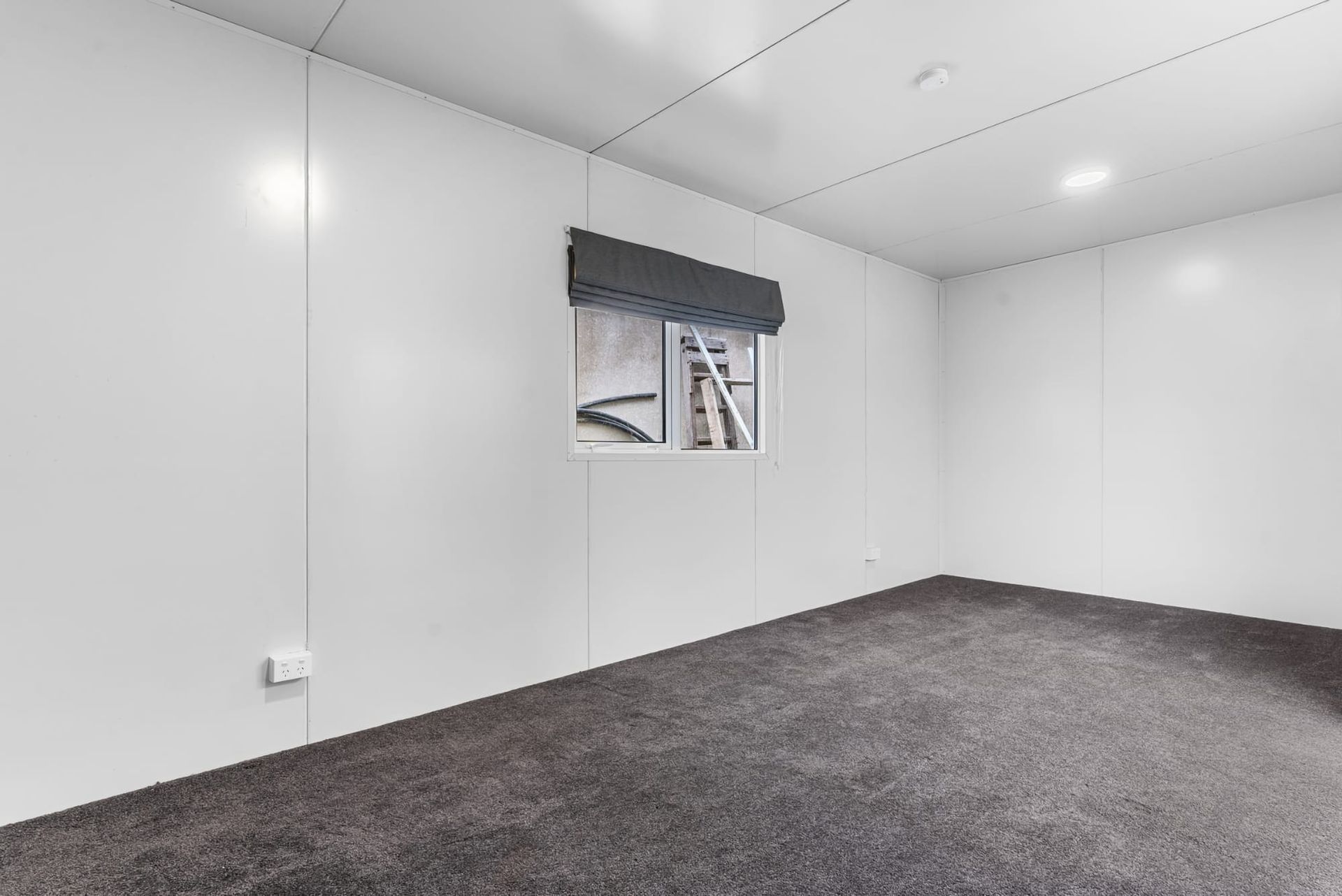Empty white room with gray carpet and a small window on the far wall