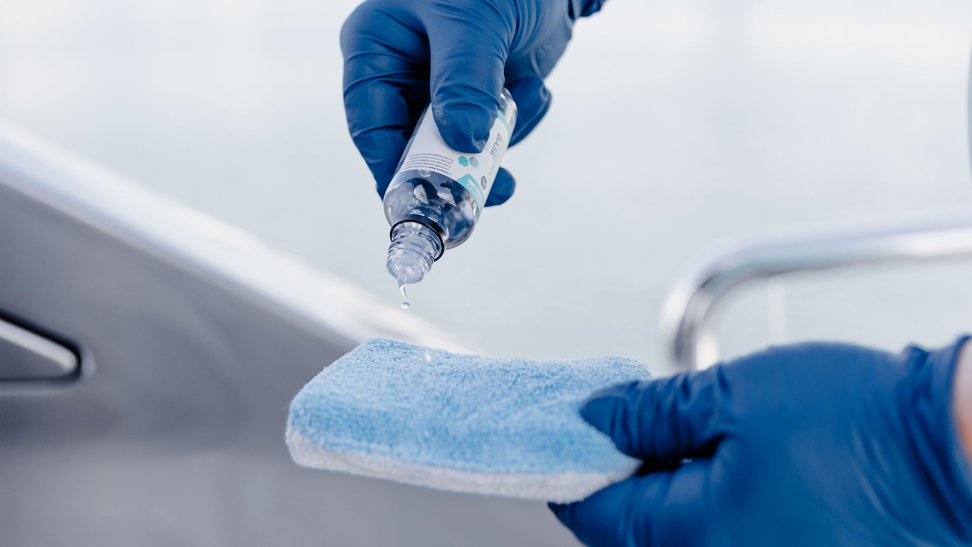 Blue-gloved hands squeeze liquid onto a sponge while cleaning a car surface.