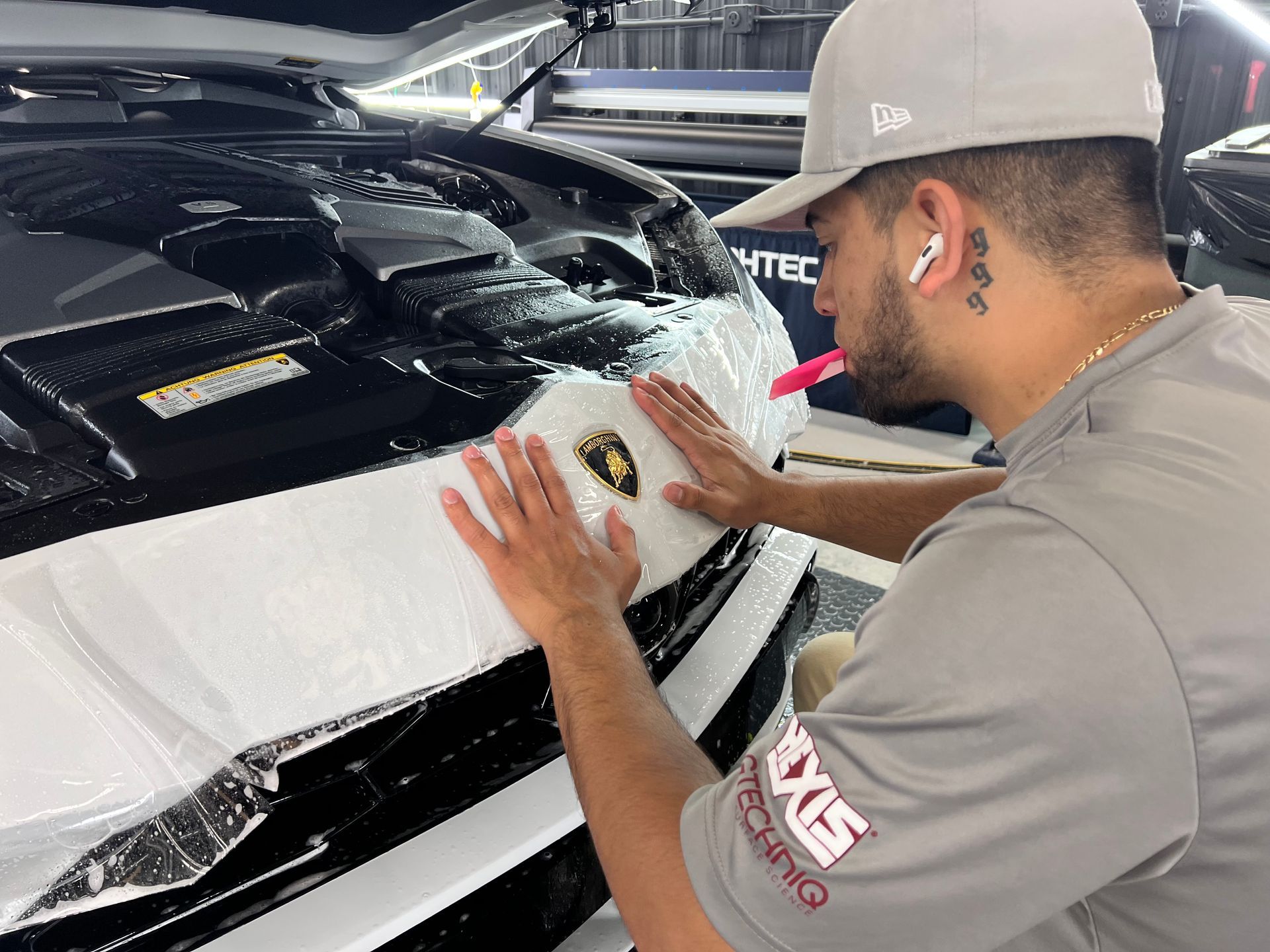 A man is applying paint protection film to the front of a Lamborghini.