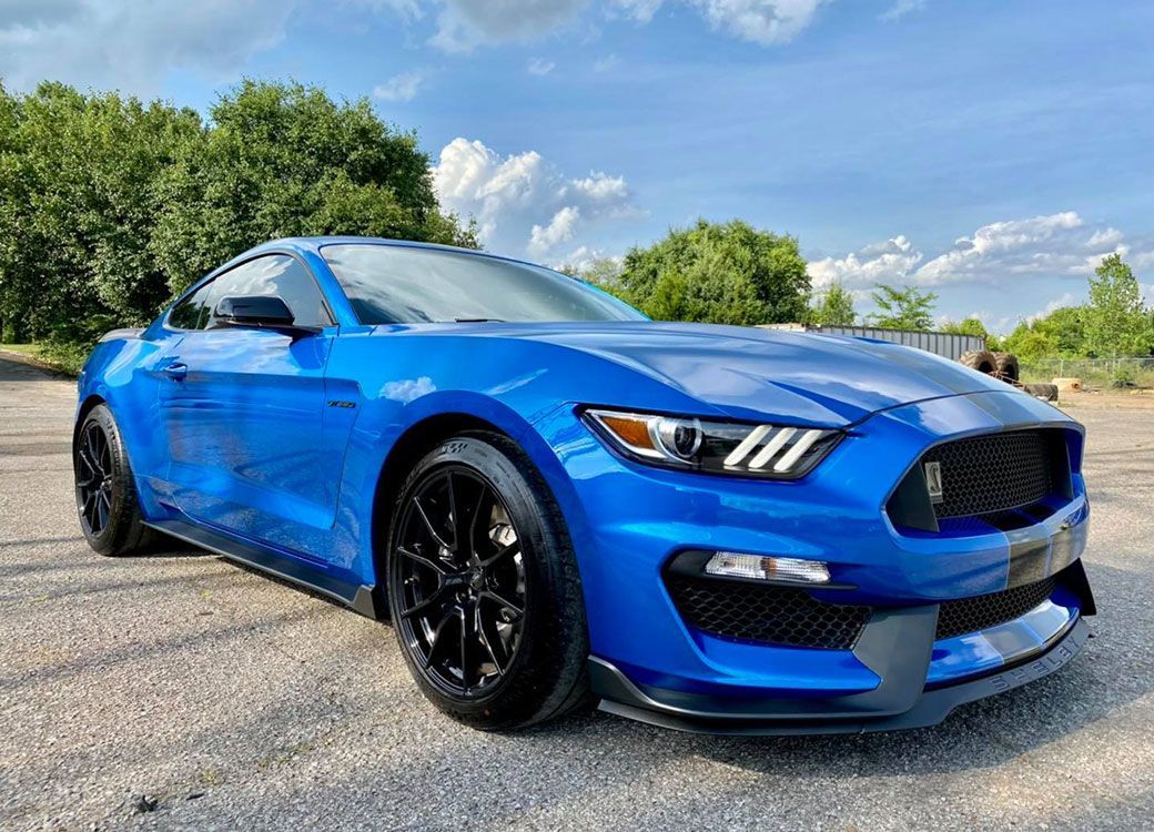 Blue Ford Mustang sports car, parked on asphalt, under a blue sky.