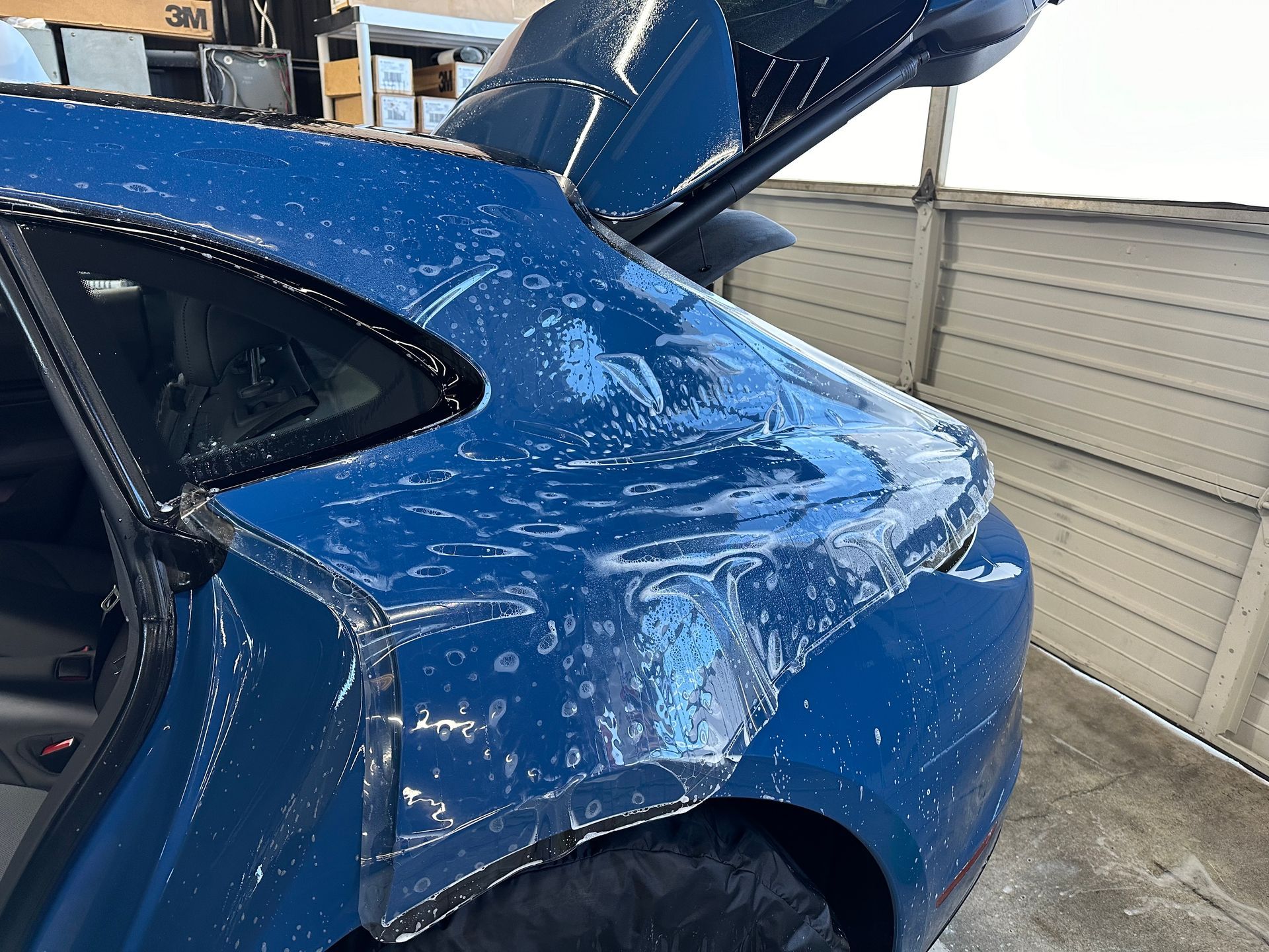A blue car with its trunk open is sitting in a garage