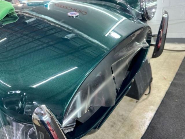 Classic dark green car with chrome accents parked indoors at an auto show