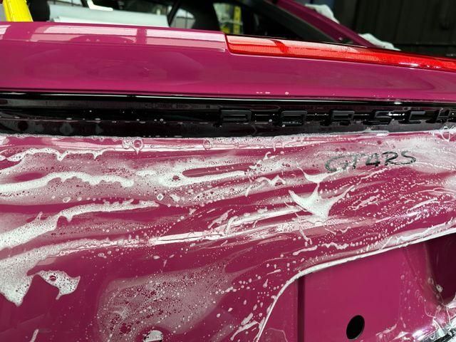 Pink car covered in soap foam during a wash, with a hand scrubbing the side panel.
