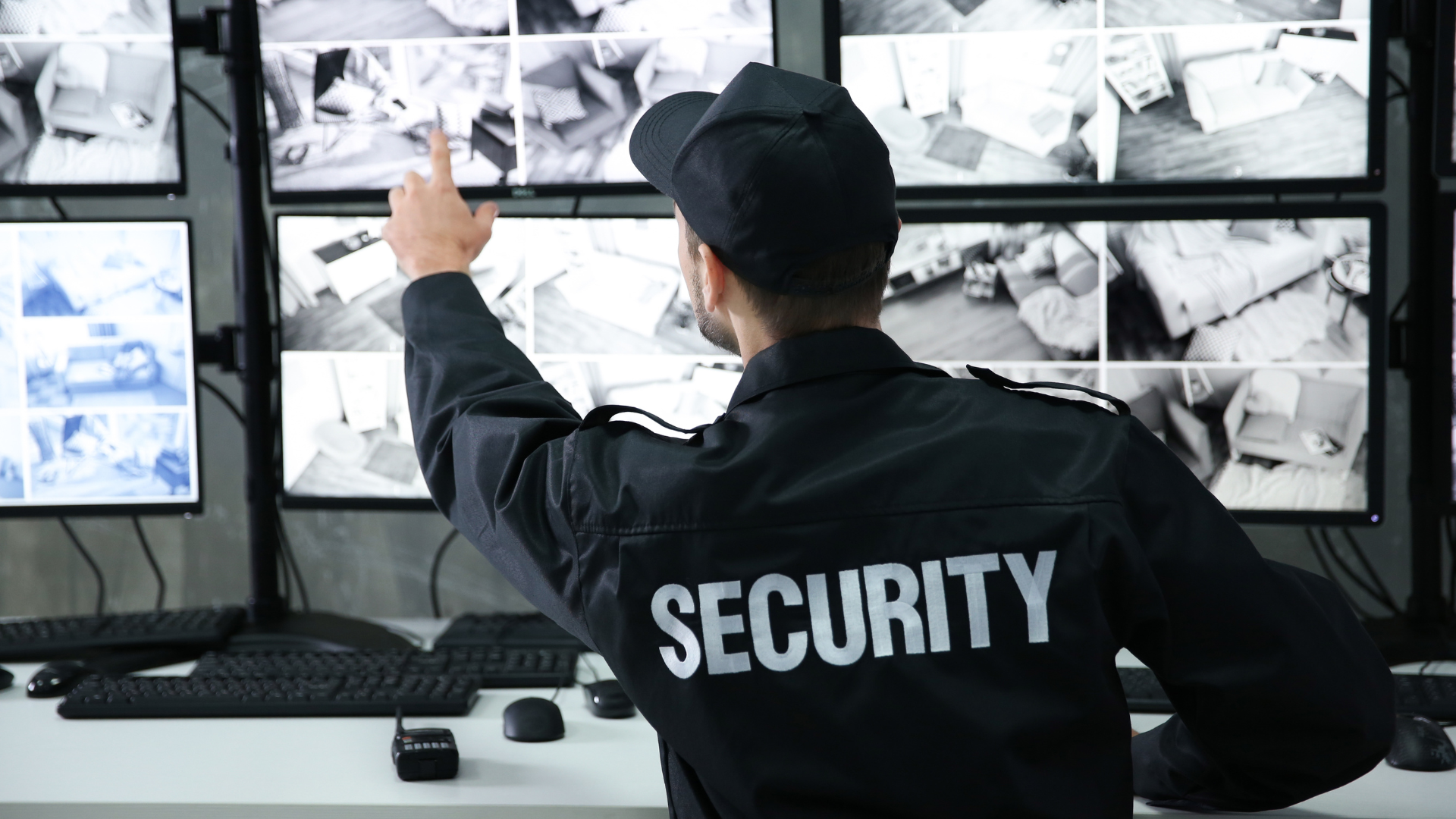 A security guard is pointing at a monitor in a control room.